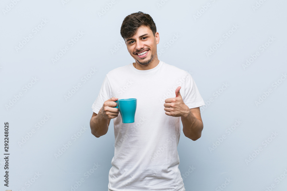 Young hispanic man holding a cup smiling and raising thumb up Young hispanic man holding a cup smiling and raising thumb up