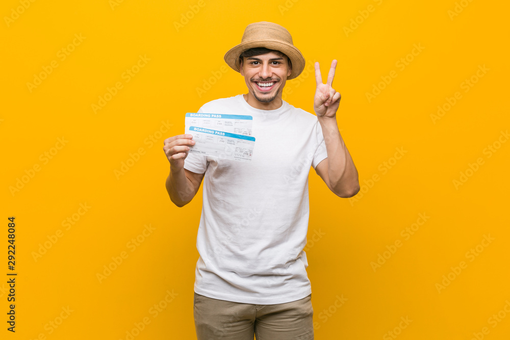 Young hispanic man holding an air tickets showing victory sign and smiling broadly.