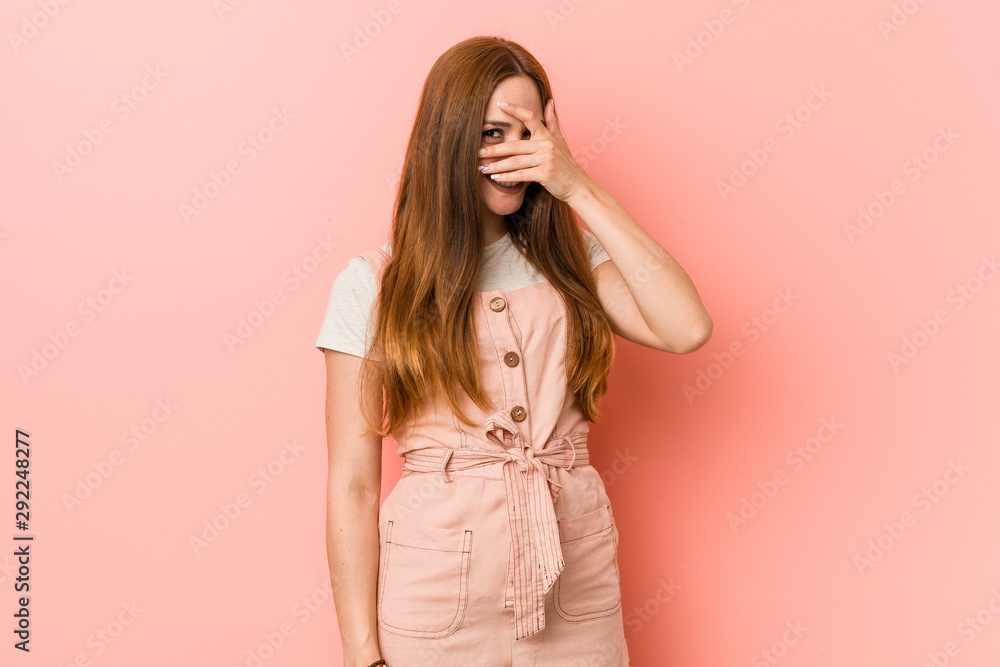 Young ginger woman with freckles blink at the camera through fingers, embarrassed covering face. Young ginger woman with freckles blink at the camera through fingers, embarrassed covering face.