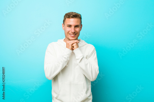 Young caucasian sport man keeps hands under chin, is looking happily aside.