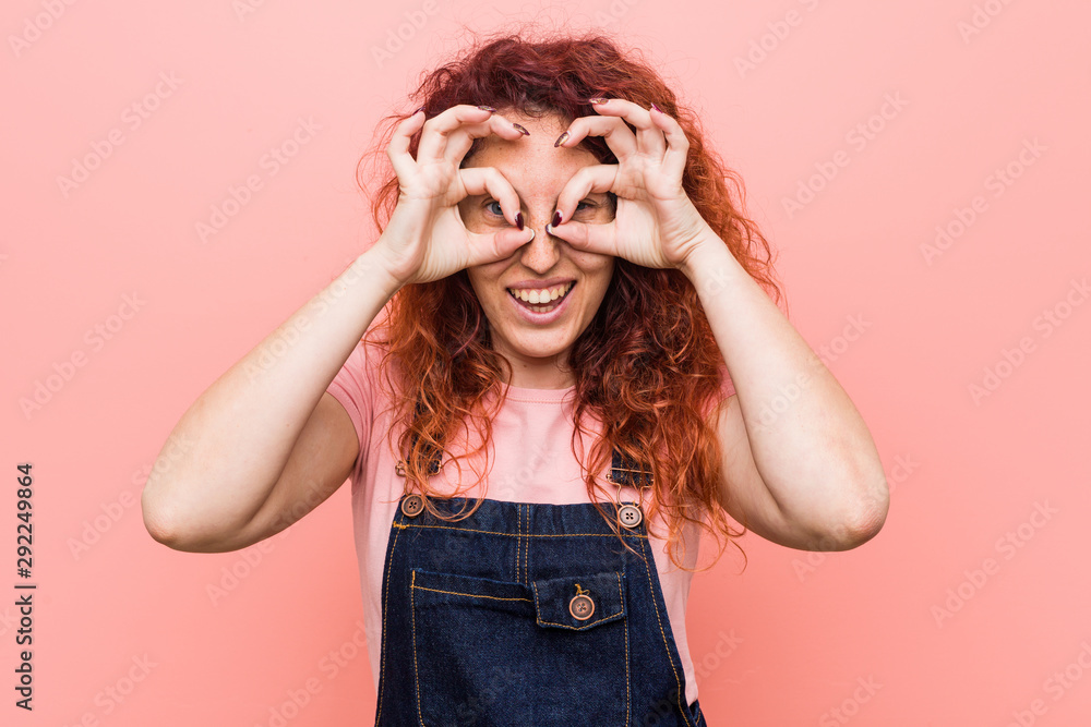 Young pretty ginger redhead woman wearing a jeans dungaree showing okay sign over eyes Young pretty ginger redhead woman wearing a jeans dungaree showing okay sign over eyes