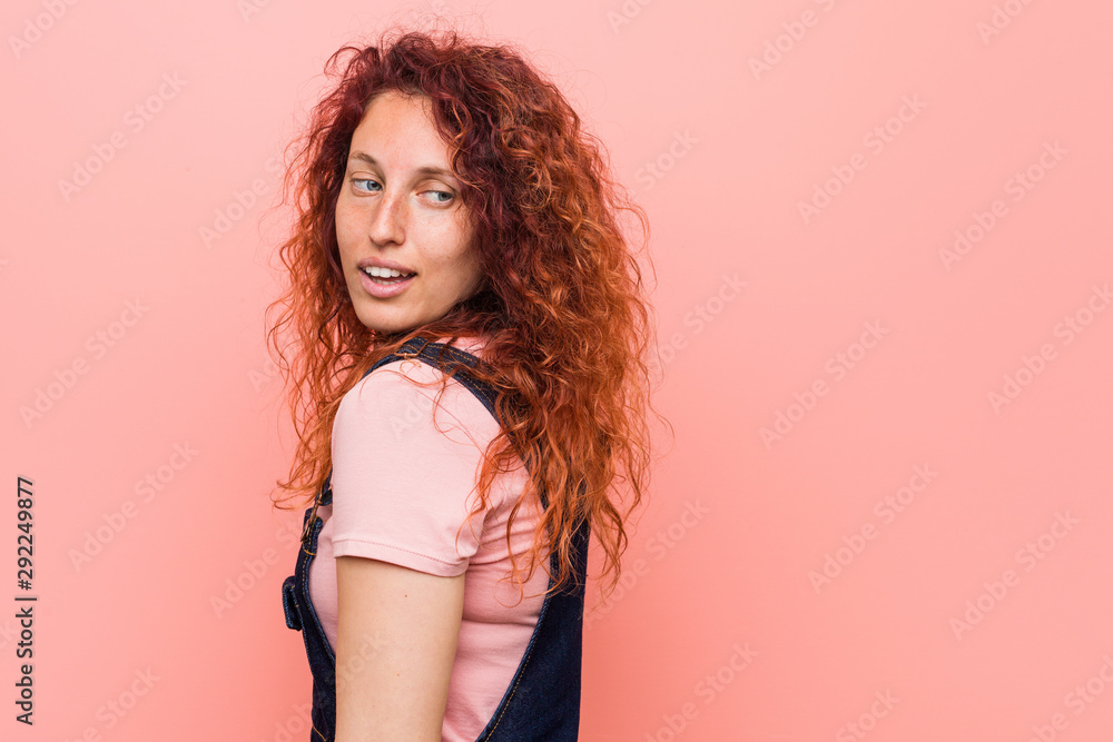 Young pretty ginger redhead woman wearing a jeans dungaree looks aside smiling, cheerful and pleasant. Young pretty ginger redhead woman wearing a jeans dungaree looks aside smiling, cheerful and pleasant.