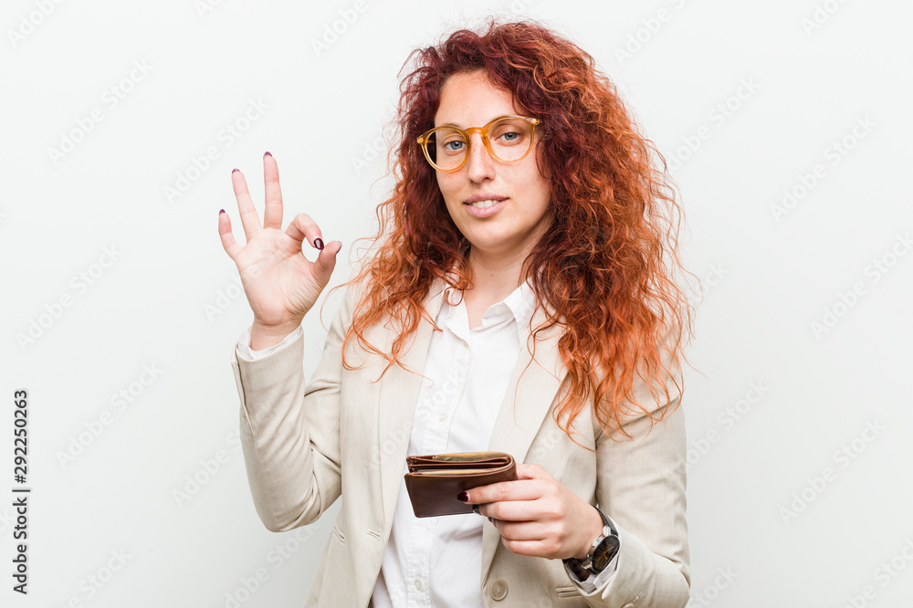 Young caucasian redhead woman holding a wallet cheerful and confident showing ok gesture. Young caucasian redhead woman holding a wallet cheerful and confident showing ok gesture.