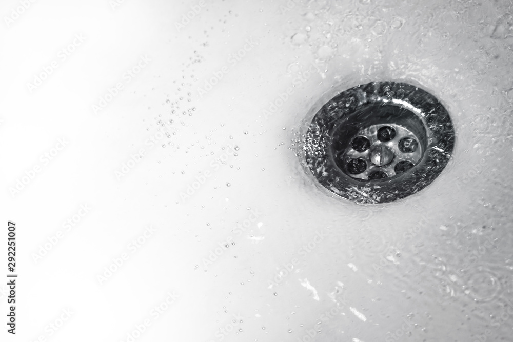 A stream of clean water flows into the drain stainless steel sink in white tones. Close up of drain and water in bathroom A stream of clean water flows into the drain stainless steel sink in white tones. Close up of drain and water in bathroom