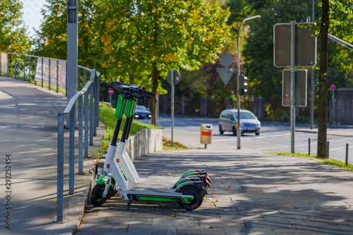 Group of E-scooters from startup company with idea of Eco friendly mobility for urban lifestyle by sharing Electric Scooter, park on shady sidewalk in Cologne, Germany.