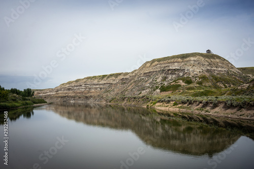 Sedimentary hills reflected in a calm lake on a partly cloudy day 