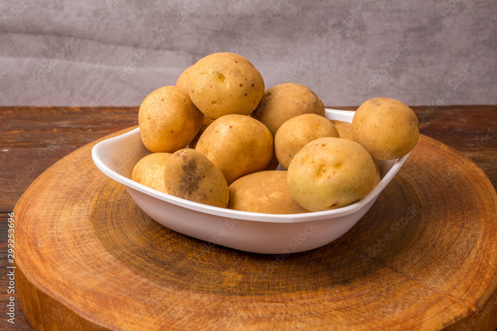 Fresh and raw potatoes stacked in a round dish on wooden table. Rustic style.. Fresh and raw potatoes stacked in a round dish on wooden table. Rustic style..