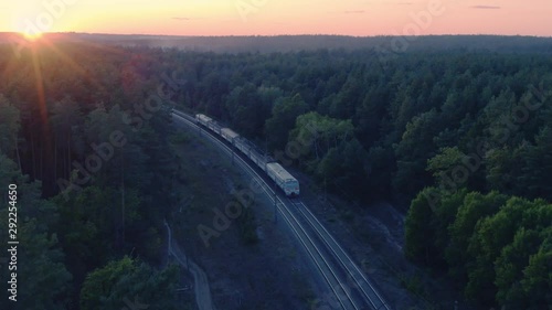 Aerial following view of the suburban train (commuter rail) rides through the autumn forest at sunset photo