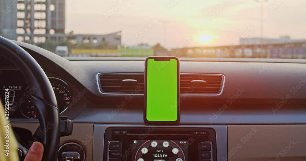 Vertical mock-up smartphone with greenscreen attached to dashboard. Close-up man driving car using mobile app in slow motion at sunset. Vertical mock-up smartphone with greenscreen attached to dashboard. Close-up man driving car using mobile app in slow motion at sunset.