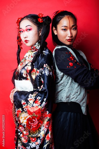 two pretty geisha girls friends: modern asian woman and traditional wearing kimono posing cheerful on red background