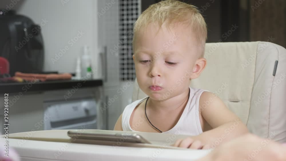 Cute little boy to drink milk for breakfast at home, while watching cartoon on tablet. Children and technology or healthy food for kid concept. Cute little boy to drink milk for breakfast at home, while watching cartoon on tablet. Children and technology or healthy food for kid concept.