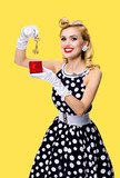 Happy smiling blond woman in pinup style black dress in polka dot, showing keys from new house, isolated over yellow
