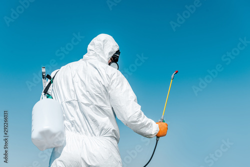 exterminator in white protective uniform holding toxic spray outside