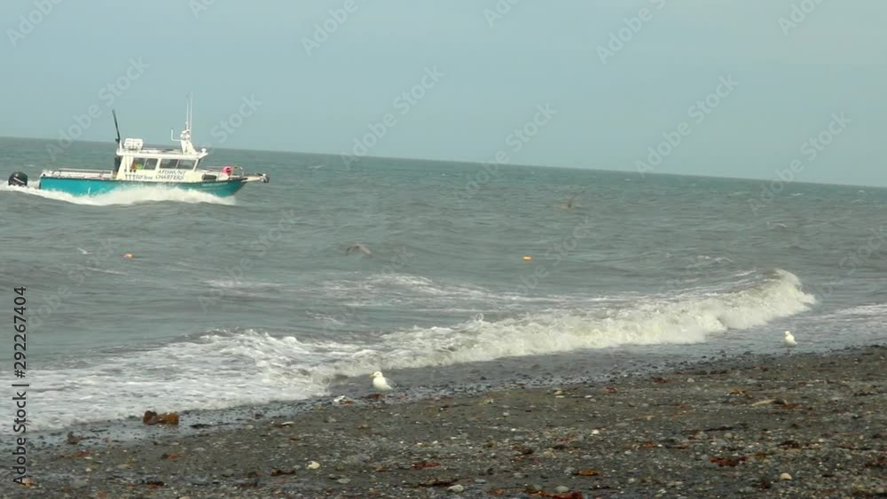 Fishing charter boat moving onto shore very fast in order to load onto a boat trailer that is waiting in the surf; once the boat is loaded onto the trailer it will be pulled from the surf in Alaska Fishing charter boat moving onto shore very fast in order to load onto a boat trailer that is waiting in the surf; once the boat is loaded onto the trailer it will be pulled from the surf in Alaska