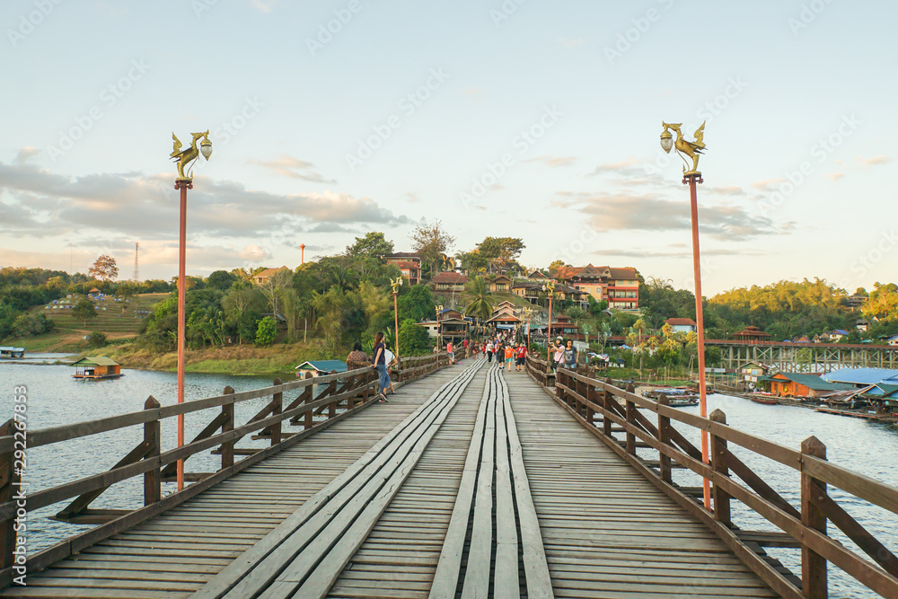 Kanchanaburi / Thailand- March 22 2019 local Mon people and tourists walk on vintage wooden bridge across river Kanchanaburi / Thailand- March 22 2019 local Mon people and tourists walk on vintage wooden bridge across river