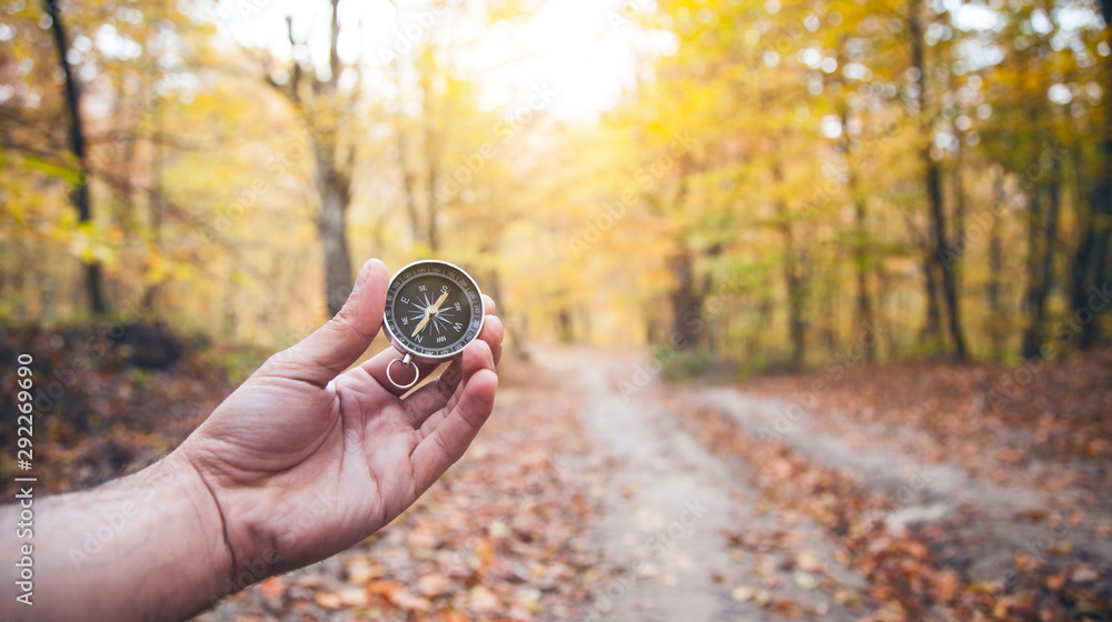 Male hand holding compass in autumn forest.
