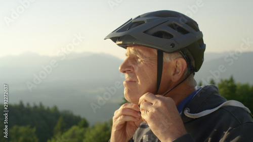CLOSE UP: Focused senior man straps up his helmet before an evening bicycle ride