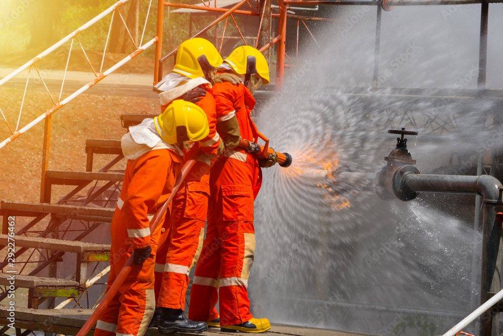 Three brave firefighters using extinguisher and water from hose for fire fighting, Firefighter spraying high pressure water to fire, Firefighter training with dangerous flames, Copy space-Image