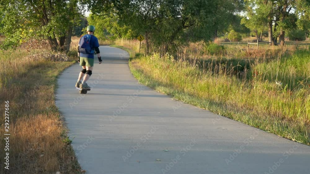 Senior man with a backpack is slowly riding an electric one-wheeled skateboard on a bike trail in early fall scenery in northern Colorado. Senior man with a backpack is slowly riding an electric one-wheeled skateboard on a bike trail in early fall scenery in northern Colorado.