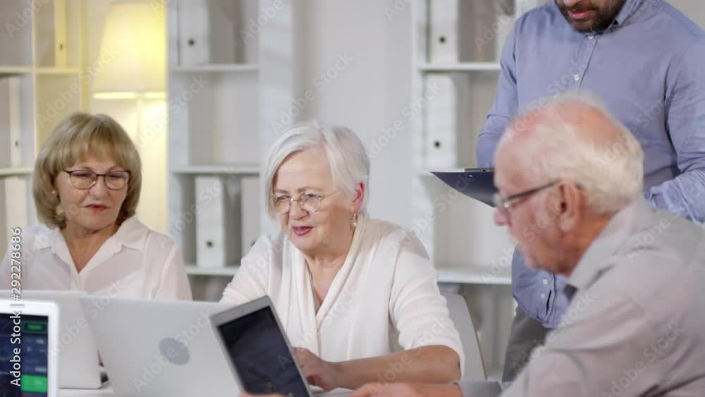 Handheld tracking shot of male teacher with clipboard looking over shoulders of elderly people Handheld tracking shot of male teacher with clipboard looking over shoulders of elderly people