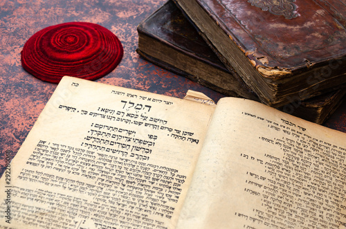 Obraz na płótnie Jewish Bible. A stack of old leather-bound Jewish books with gold stamping and red knitted jewish bale. One book is open. Closeup of Hebrew text. Selective focus w salonie