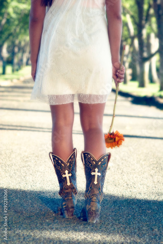 young woman walking on the street in cowboy boots with sunflower