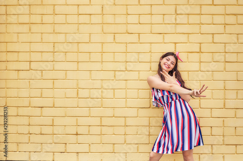 close-up young woman in a summer dress with a pink bow emotionally fun posing on a background of a yellow brick wall. copy space