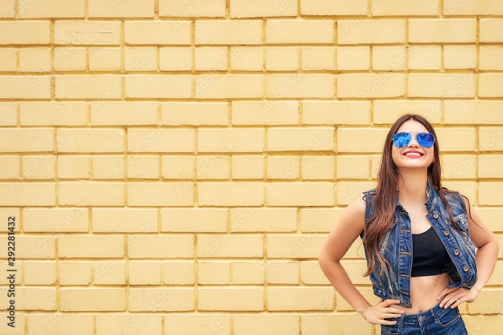 cheerful hipster girl going crazy making funny face and showing her tongue. yellow urban wall background. copy space