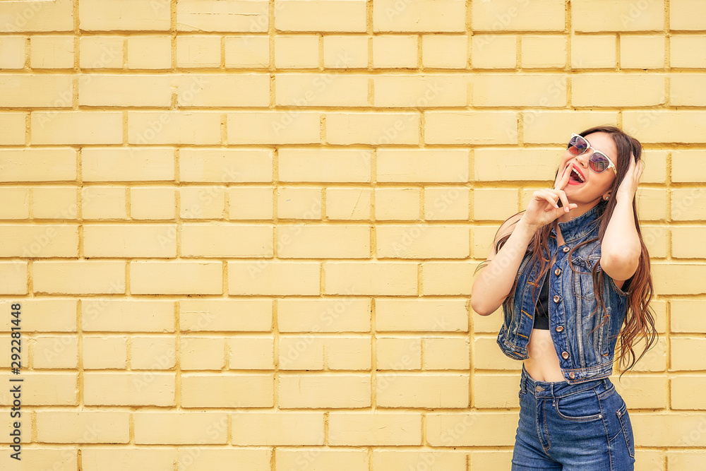 Hipster girl emotionally posing on a background of yellow brick wall. copy space
