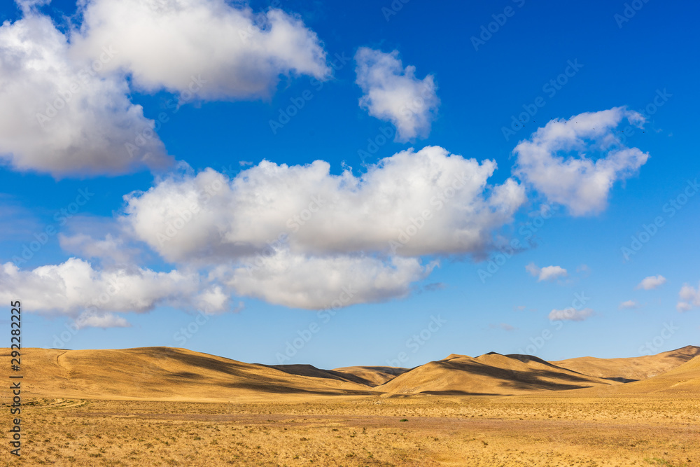 Clouds on a blue sky over mountains with dried yellow grass