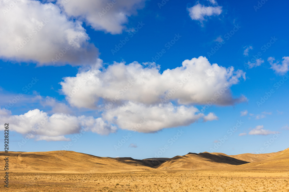 Fototapeta premium Clouds on a blue sky over mountains with dried yellow grass