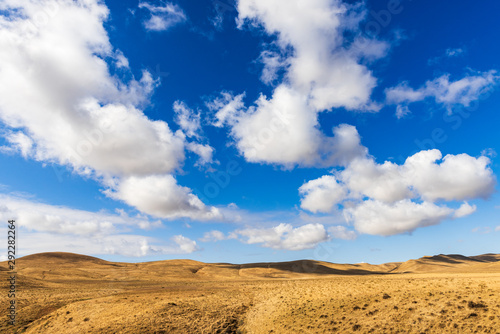 Clouds on a blue sky over mountains with dried yellow grass