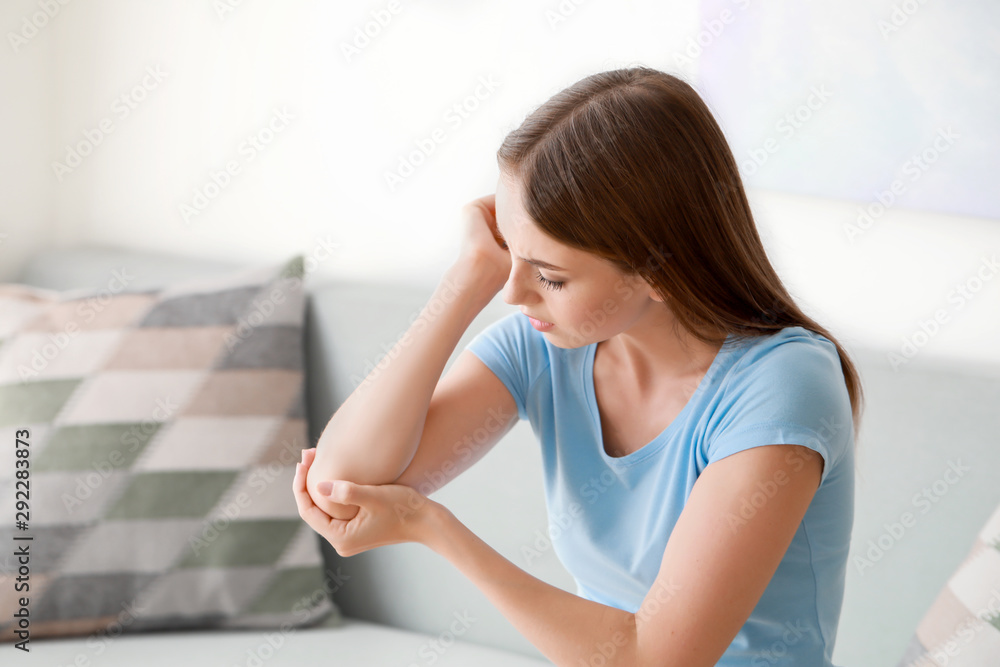 Young woman suffering from pain in elbow at home