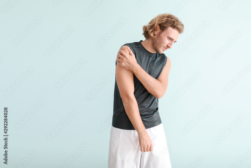 Young man suffering from pain in shoulder on color background Young man suffering from pain in shoulder on color background
