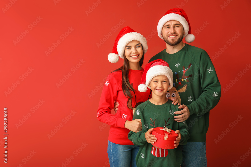 Happy family in Christmas sweaters and Santa hats on color background Happy family in Christmas sweaters and Santa hats on color background
