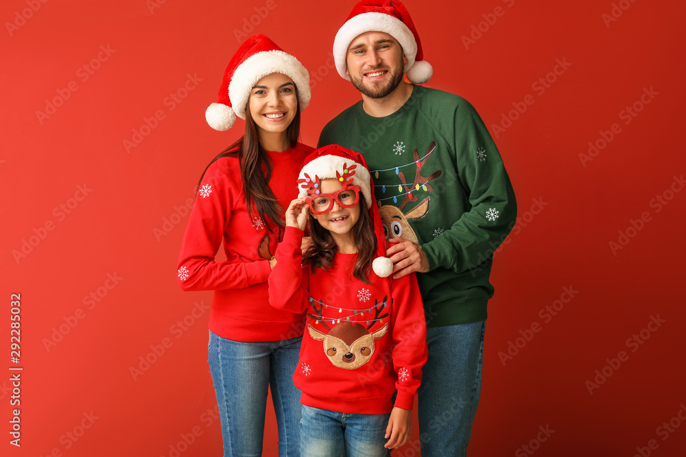 Fototapeta premium Happy family in Christmas sweaters and Santa hats on color background
