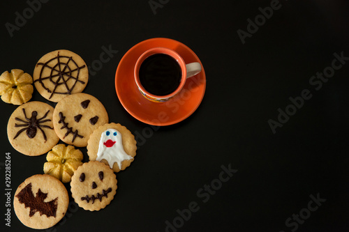 Homemade cakes for Halloween.  A Cup of coffee, terribly tasty cookies with terrible emoticons, cobwebs, spiders, bats, pumpkins on a black background. photo