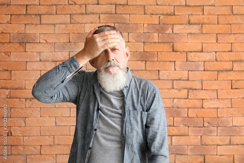 Senior man suffering from headache against brick wall Senior man suffering from headache against brick wall