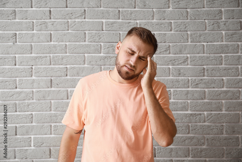 Young man suffering from headache against grey brick wall Young man suffering from headache against grey brick wall