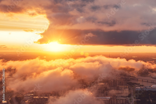 Beautiful aerial view sunset over the city and low floating clouds and the bright sun on the horizon.