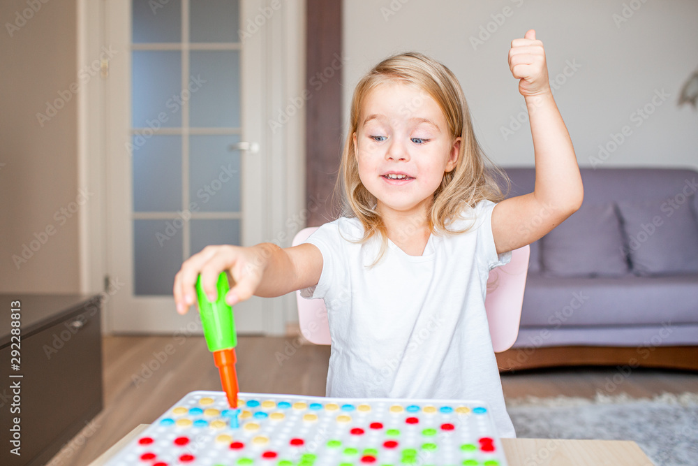 Happy pretty little blonde girl sitting at a table at home playing with a toy screwdriver and multicolor screws. Early education. Happy pretty little blonde girl sitting at a table at home playing with a toy screwdriver and multicolor screws. Early education.