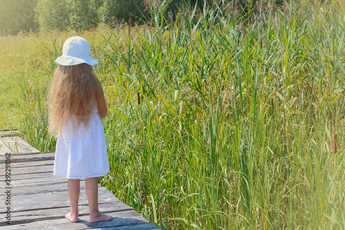 Little girl stands with his back on a bridge near a pond © lexashka