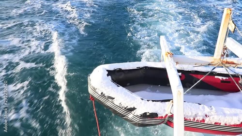 Liferaft covered with snow at the back of a fishing boat with the trail of the boat in the ocean in the background. photo