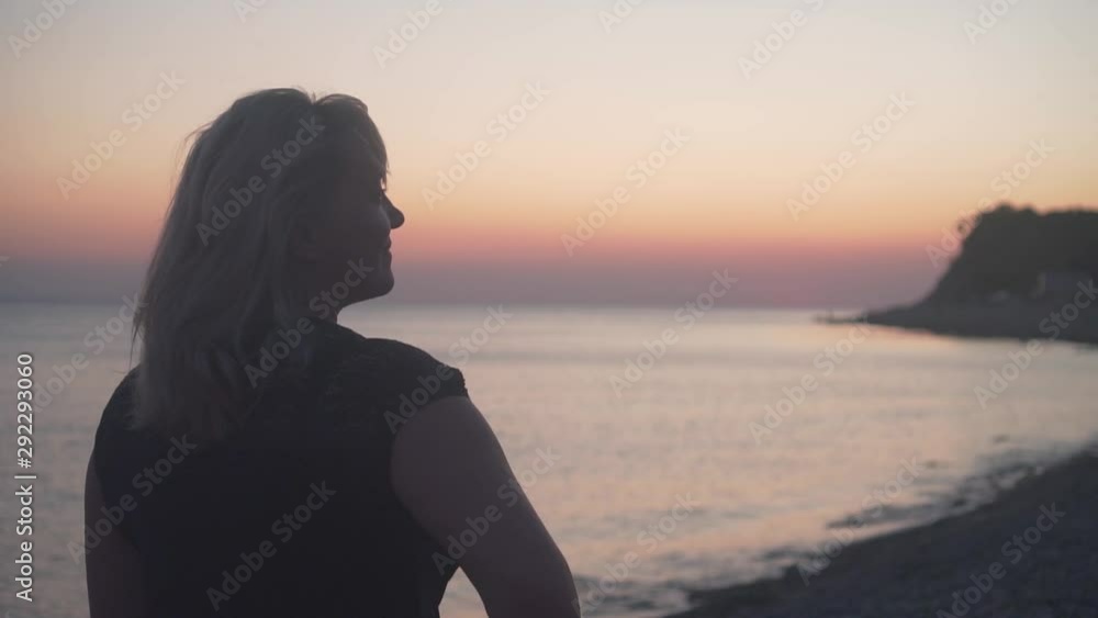 A woman stands on a background of sea sunset. A woman stands with her back to the camera, stands on the beach. A woman is standing at sea sunset. A woman stands on a background of sea sunset. A woman stands with her back to the camera, stands on the beach. A woman is standing at sea sunset.