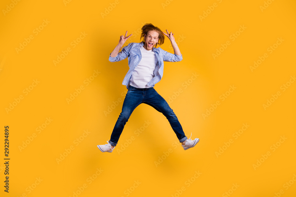 Full length body size photo of shouting crazy ecstatic overjoyed guy jumping up wearing jeans denim sneakers isolated over bright color background showing you v-sign