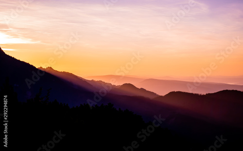 Romantic purple and orange sunset over the high Tatra mountains with dense mist and long sun rays