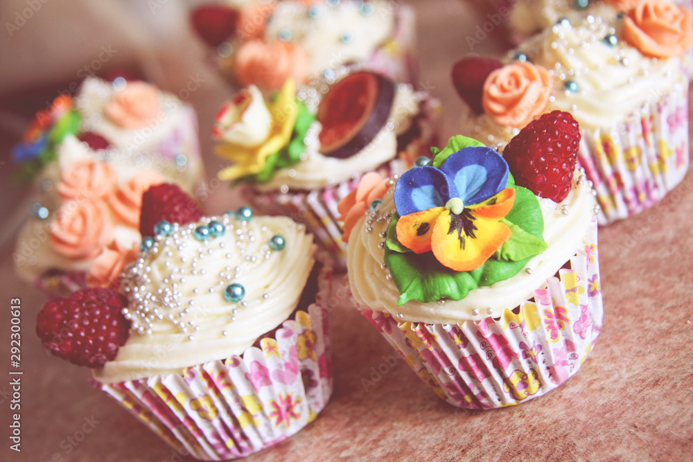 Close up view on decorated party cupcakes. Colorful cupcake flower icing and raspberry decoration. 