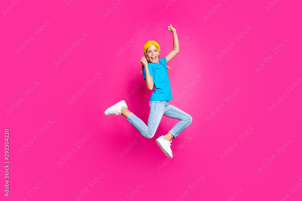 Full length photo of crazy funny kid raise fists scream yeah jump ecstatic see incredible discounts for spring vacations wear blue yellow clothes denim jeans sneakers isolated pink color background