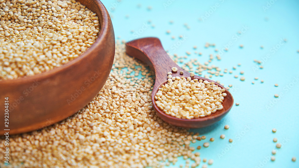 White quinoa seeds on a blue background. quinoa in bowl and a spoon on kitchen table top view. Healthy and diet superfood product. White quinoa seeds on a blue background. quinoa in bowl and a spoon on kitchen table top view. Healthy and diet superfood product.