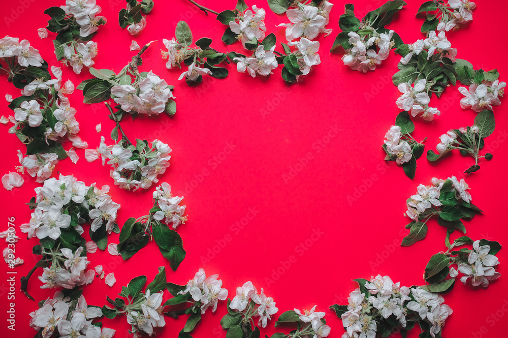 Frame of white blossoming apple trees and green leaves on a red background made of pastel paper. Copy space and space to insert text. Natural vignette. Very bright and saturated colors. Psychedelic. Frame of white blossoming apple trees and green leaves on a red background made of pastel paper. Copy space and space to insert text. Natural vignette. Very bright and saturated colors. Psychedelic.